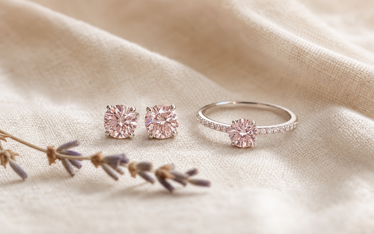 Pink diamond stud earrings and a matching solitaire ring resting on cream linen